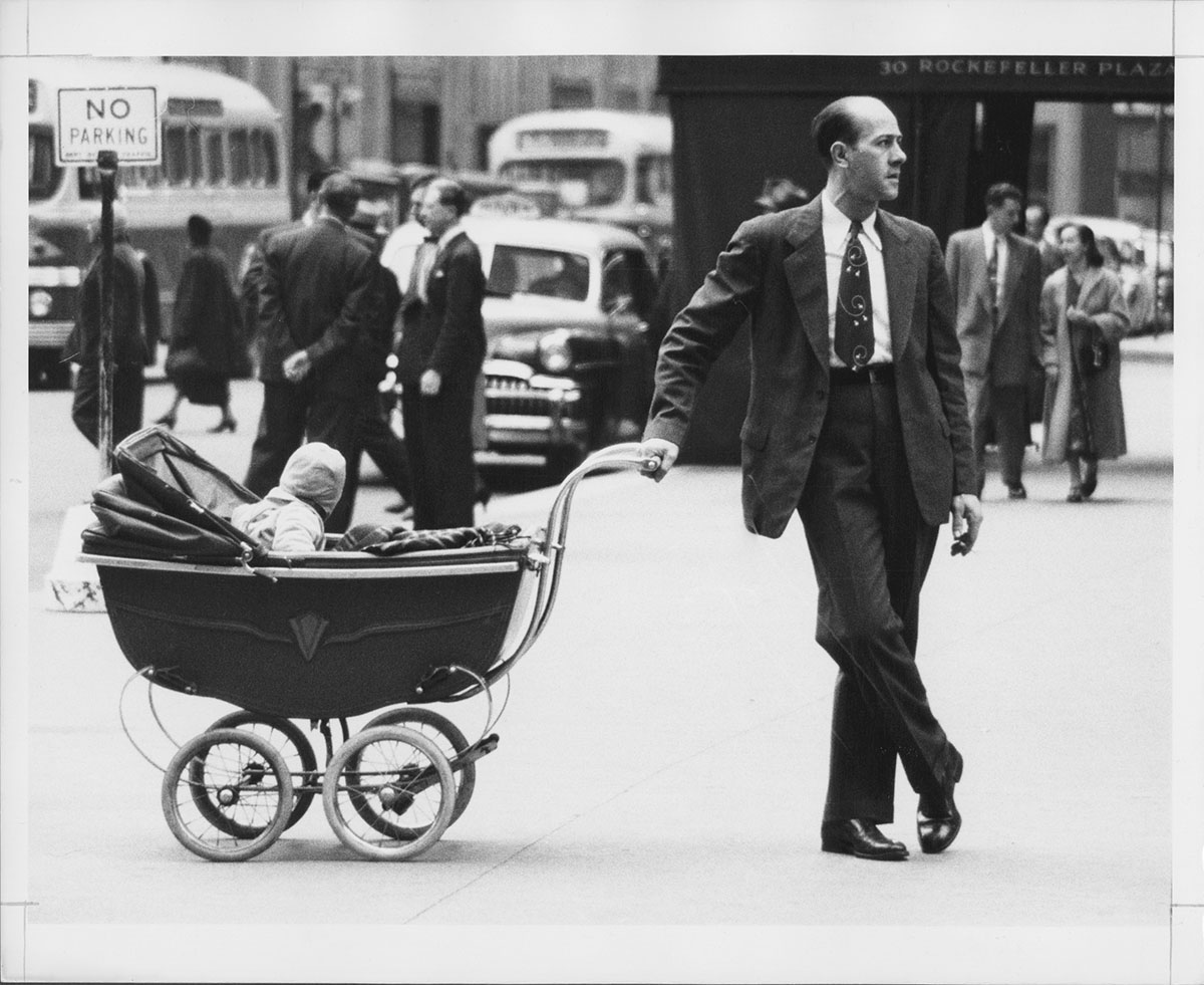 Man standing on sidewalk with one hand on baby carriage, 1953, Anthony Angel